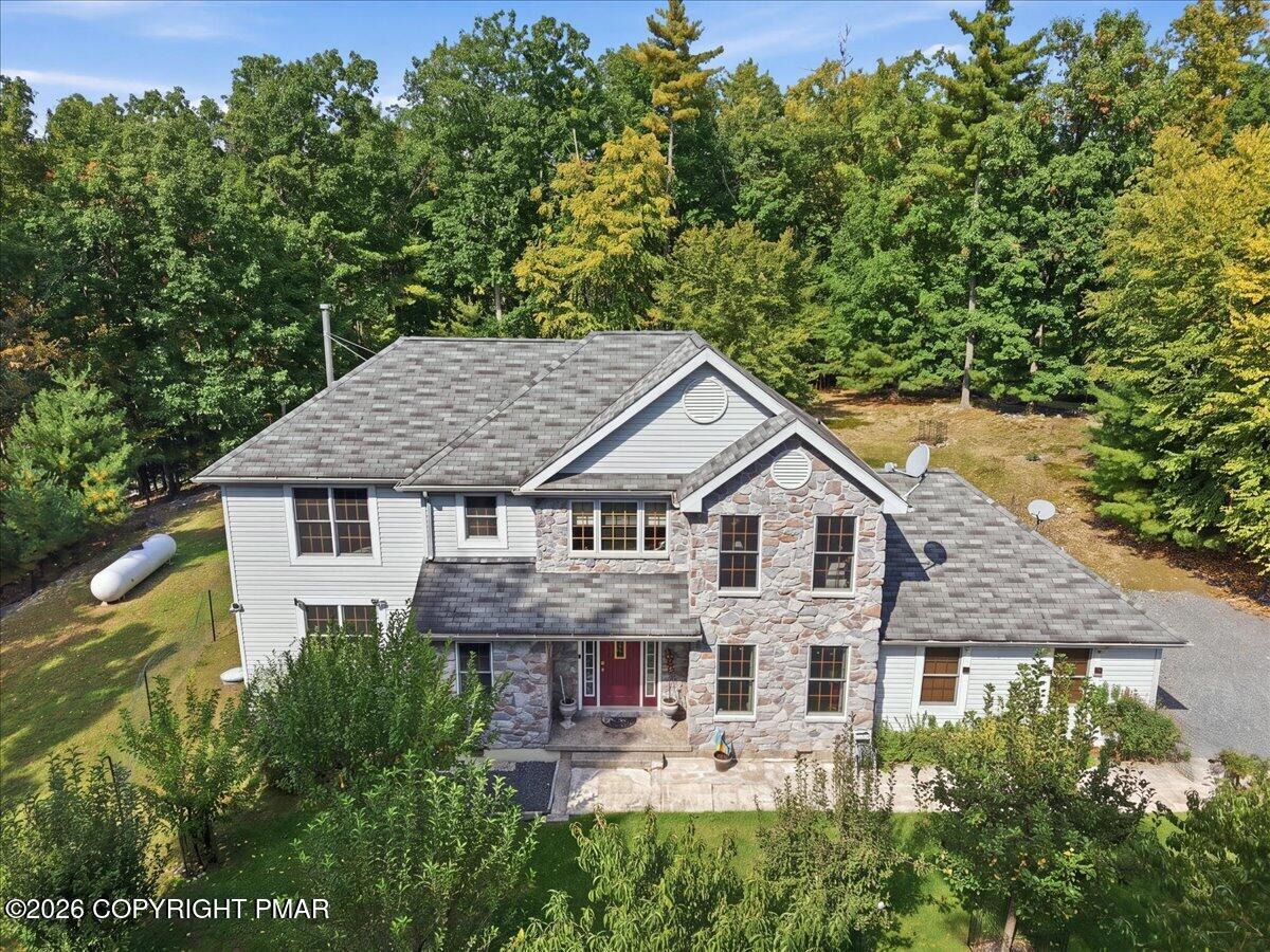 Aerial view of a two-story home with a stone facade and mature trees.