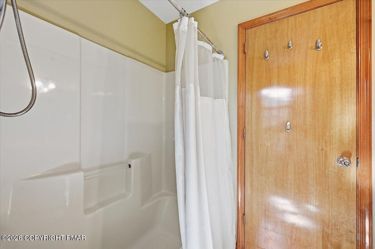 Bathroom shower and tub beside a wooden door with hooks.