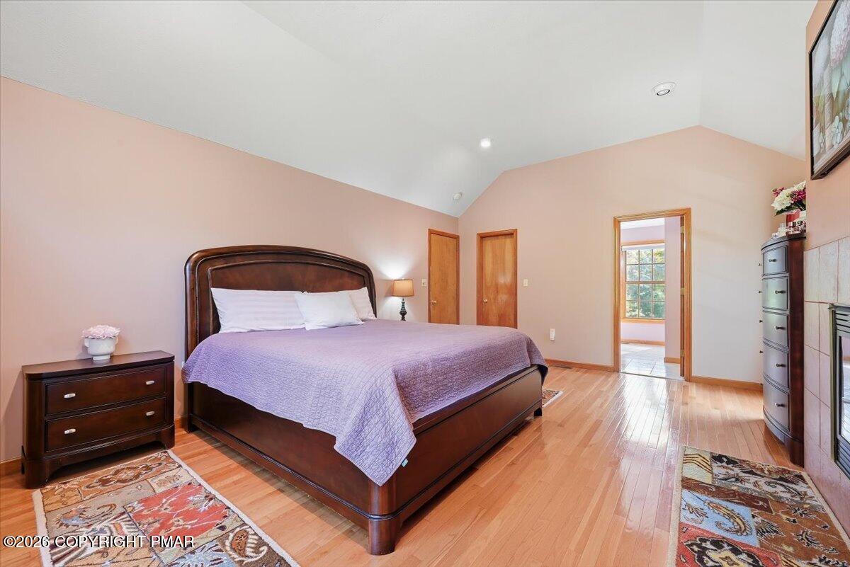 Bedroom with a dark wood bed, lavender bedding, hardwood floors, and a high sloped ceiling.