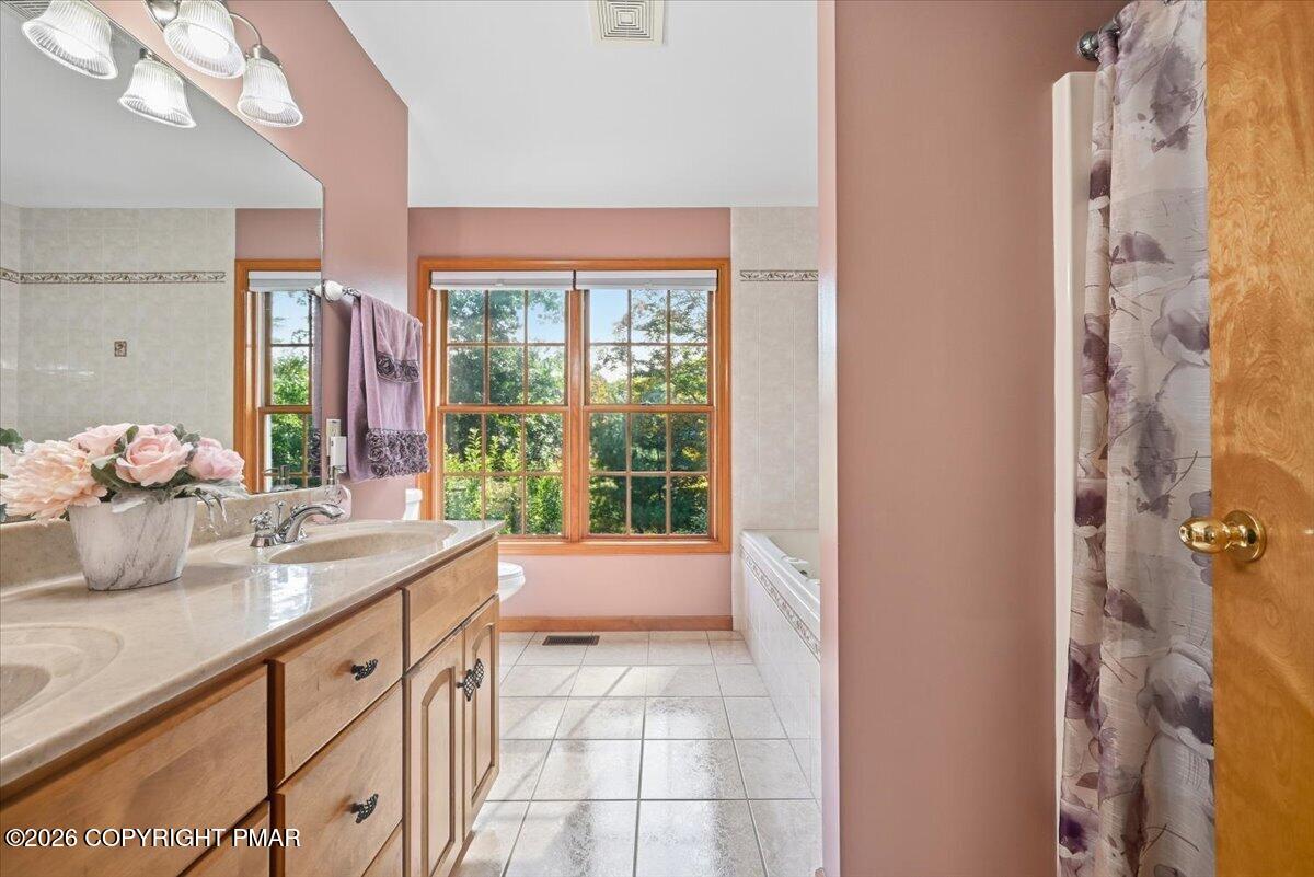 Bathroom with a long wood vanity, tiled floor, bathtub, and large windows overlooking trees.