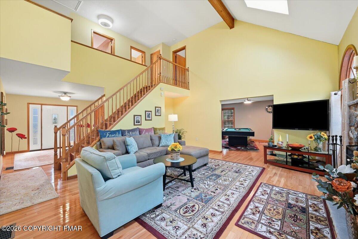 Double-height living room with a wooden staircase, skylight, sectional sofa, and view into a pool-table room.