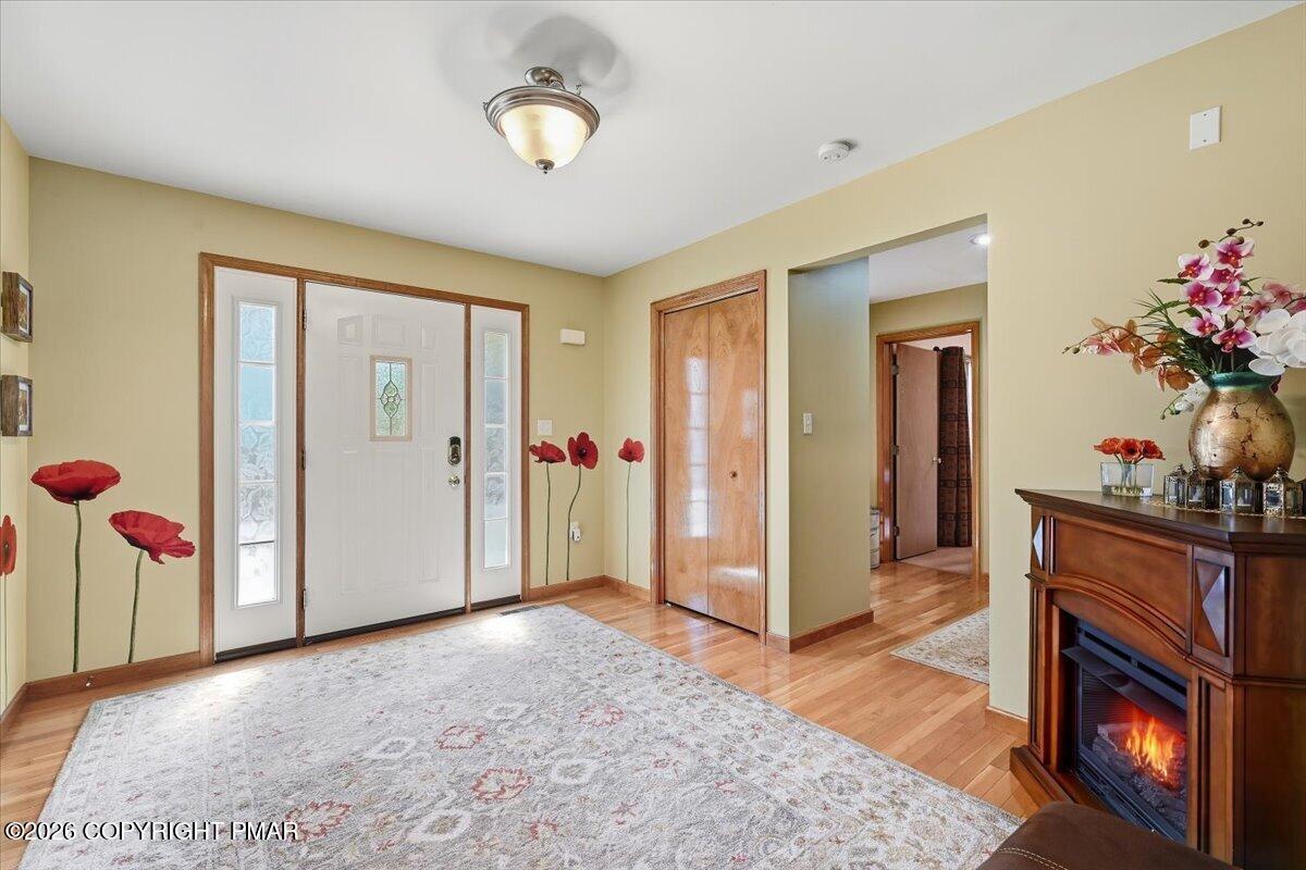 Entry foyer with a white front door, hardwood floors, patterned rug, and a wooden cabinet fireplace.