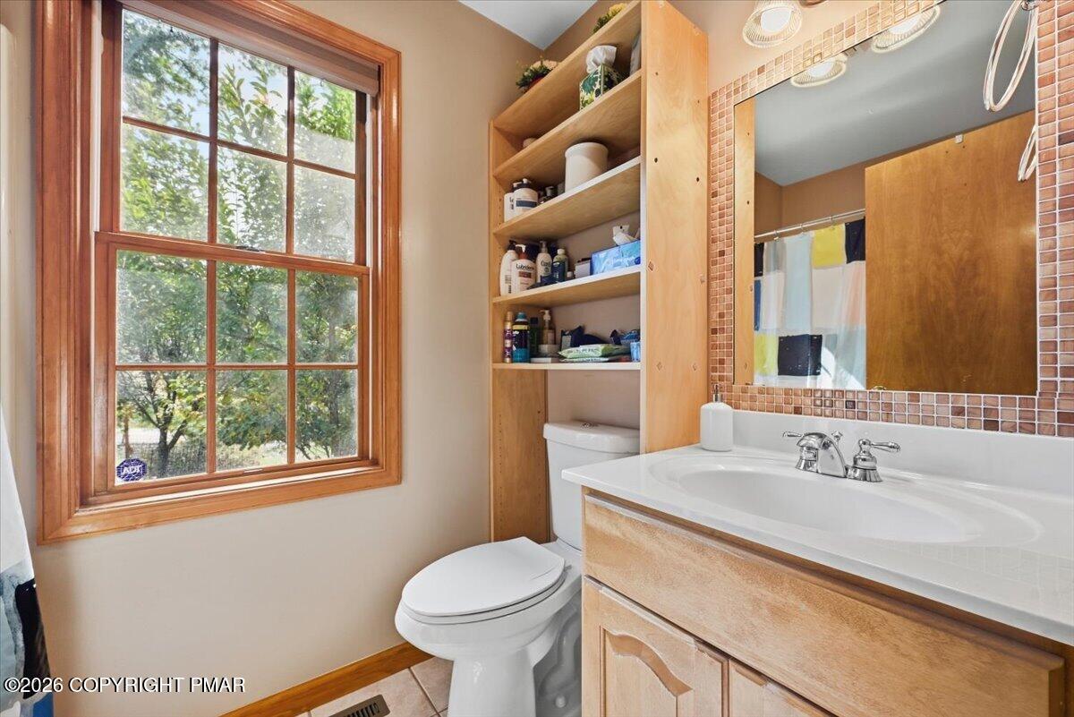 Bathroom with a wooden vanity, built-in shelving, and a large window overlooking trees.