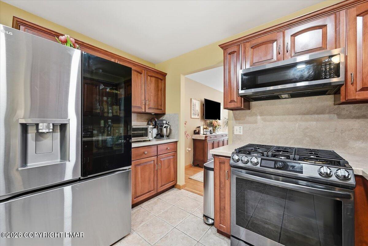 Kitchen with reddish wood cabinets, stainless appliances, and a prominent gas range.