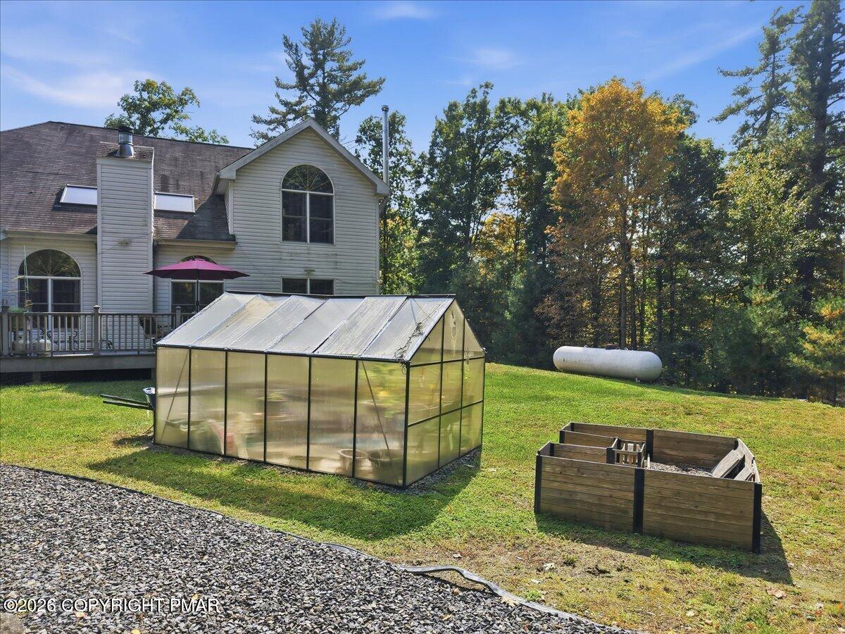 Home’s rear exterior with a deck, greenhouse, and raised garden beds in a tree-lined yard.