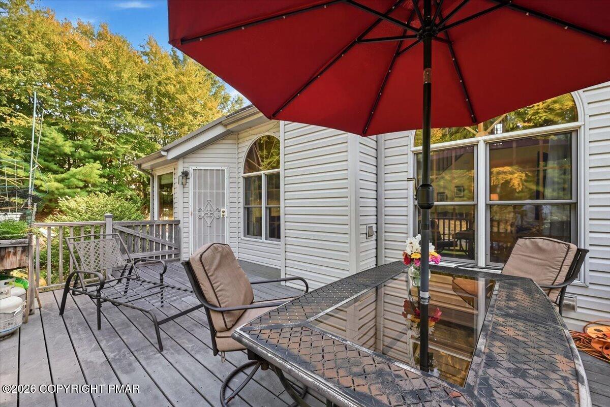 Furnished deck with a glass-top patio table and red umbrella beside the home.