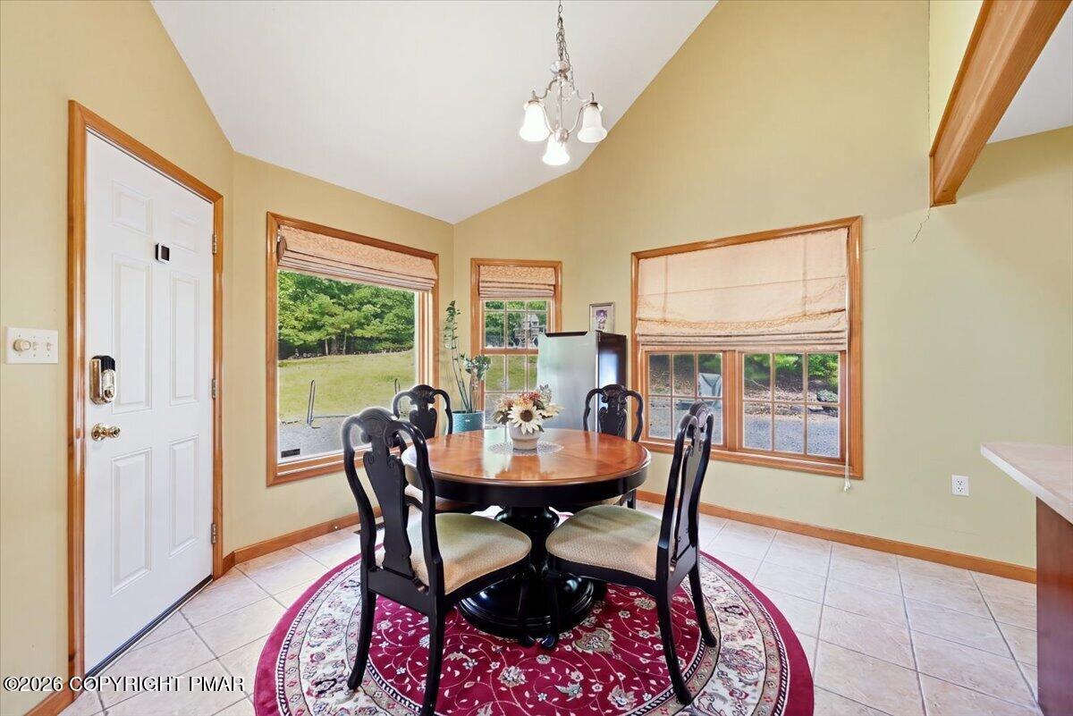 Dining area with a round wooden table, patterned rug, and large windows overlooking the yard.
