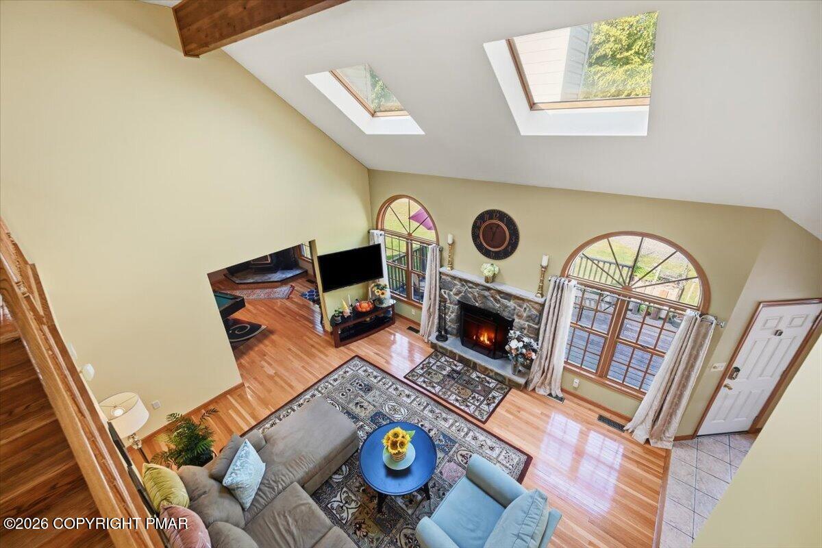 Living room with vaulted skylit ceiling, stone fireplace, arched windows, and hardwood floors.