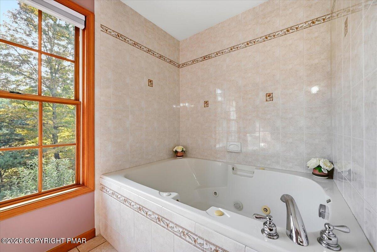 Tiled bathroom with a jetted bathtub beside a large wood-trimmed window.