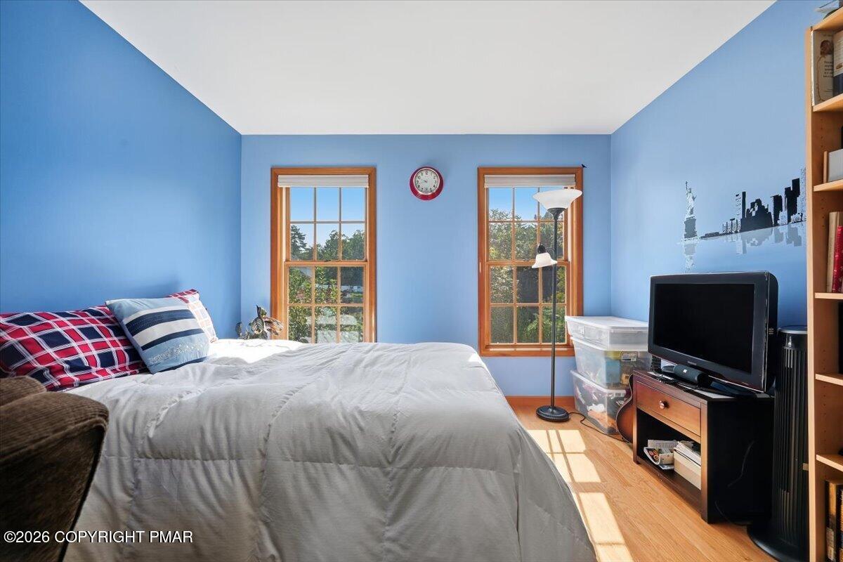 Bedroom with blue walls, a large white bed, plaid pillows, and two wood-trimmed windows.