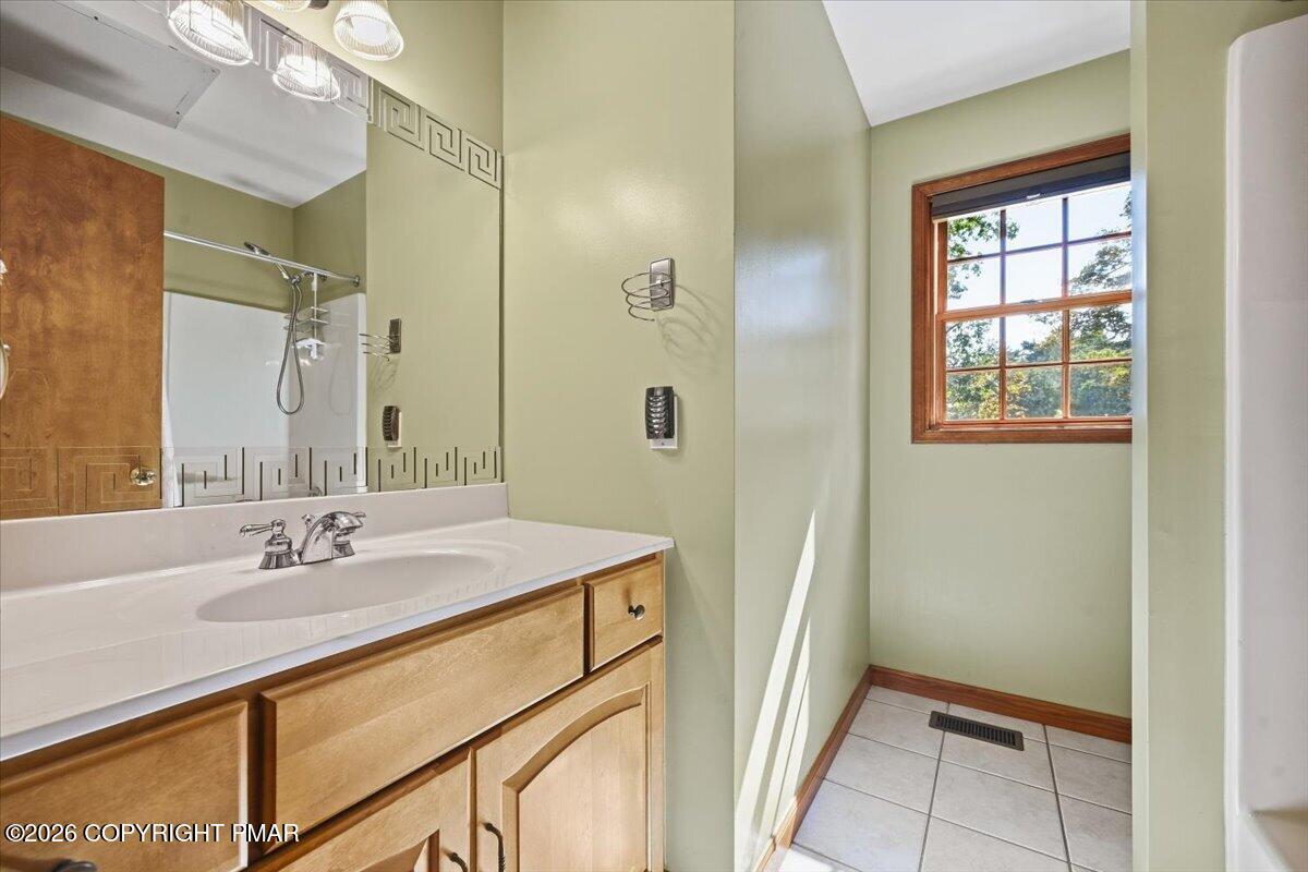 Bathroom with a wood vanity, large mirror, tiled floor, and sunlit wood-framed window.