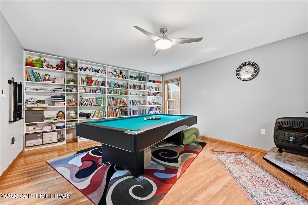 Recreation room with a teal pool table, colorful rug, and wall of bookshelves filled with books and toys.