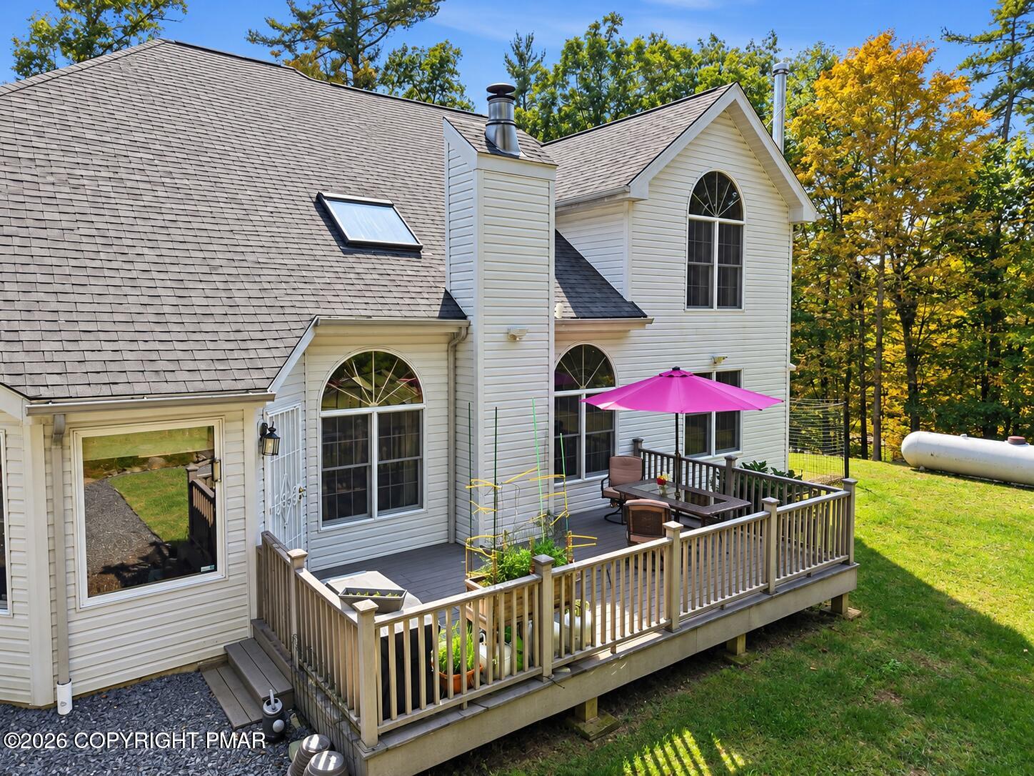 Rear of a white two-story house with a raised deck and bright pink patio umbrella.