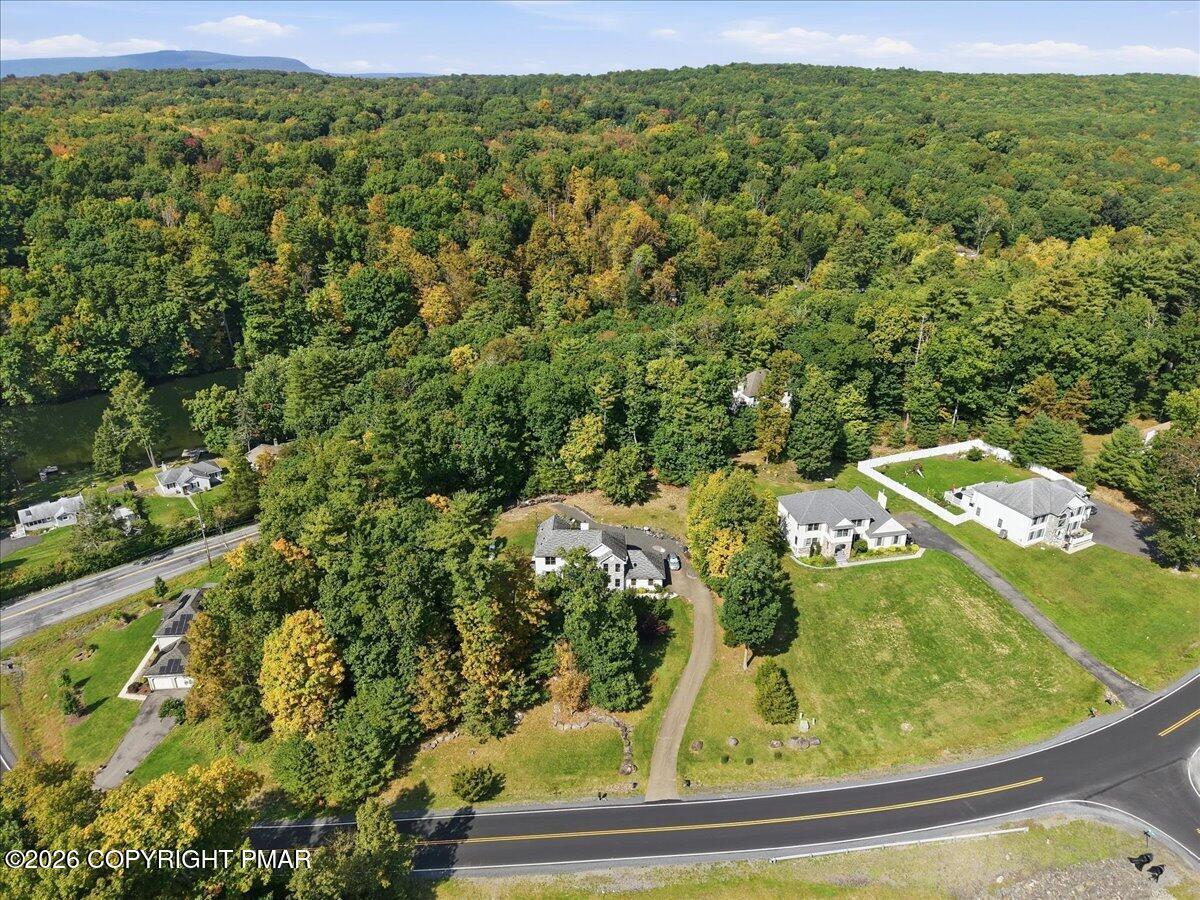 Aerial view of a home with a curved driveway beside a wooded hillside and neighboring houses.