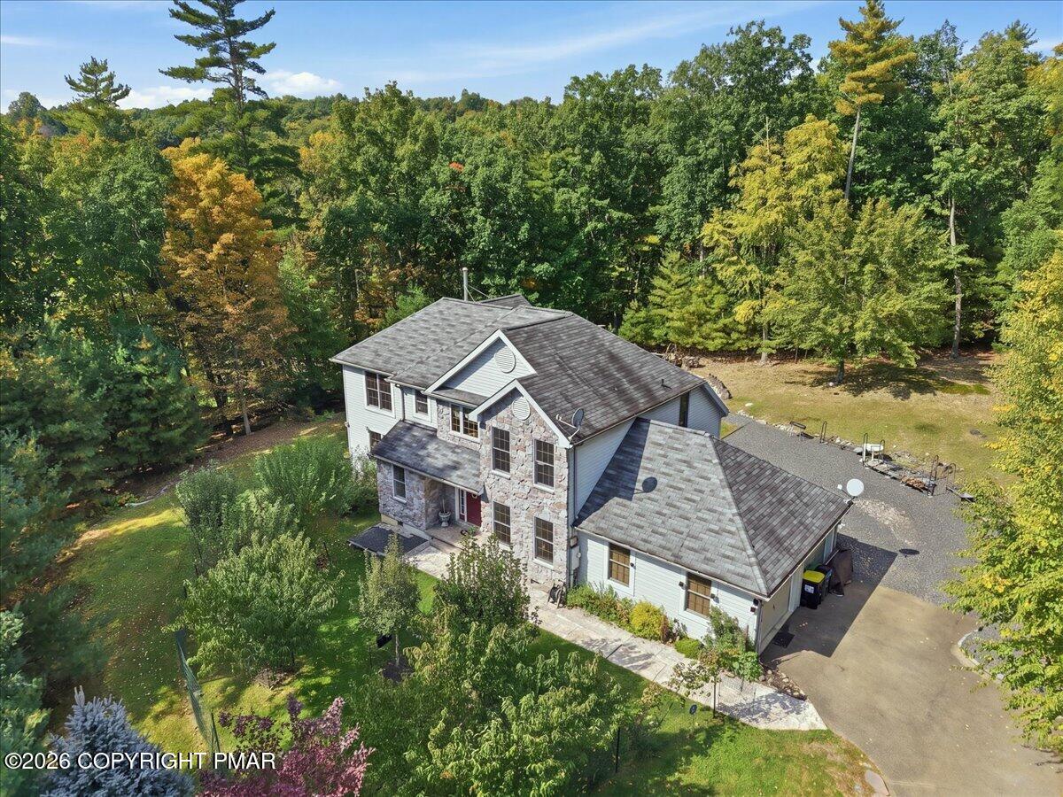 Aerial view of a stone-front house surrounded by mature trees, gardens, and a paved driveway.