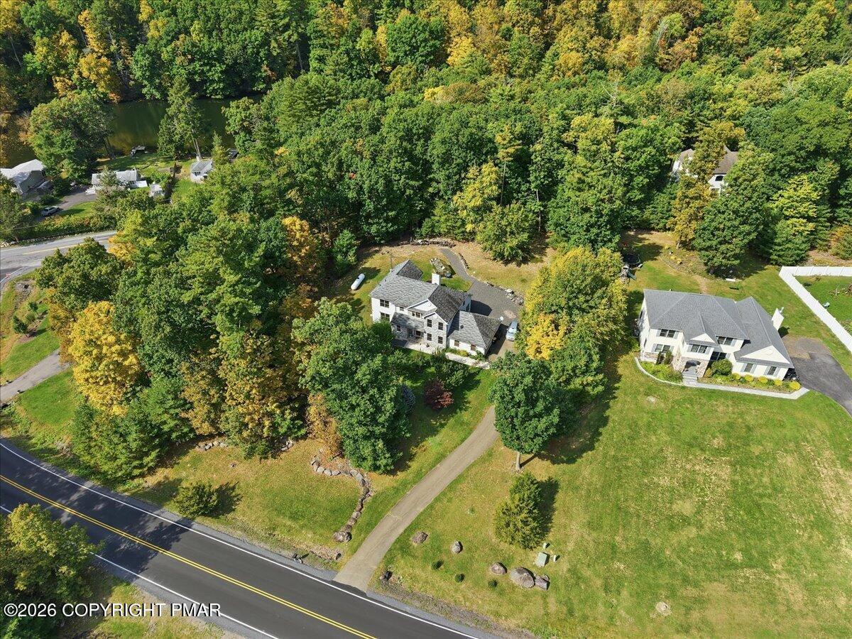 Aerial view of a home surrounded by autumn trees, with a broad grassy yard and driveway.