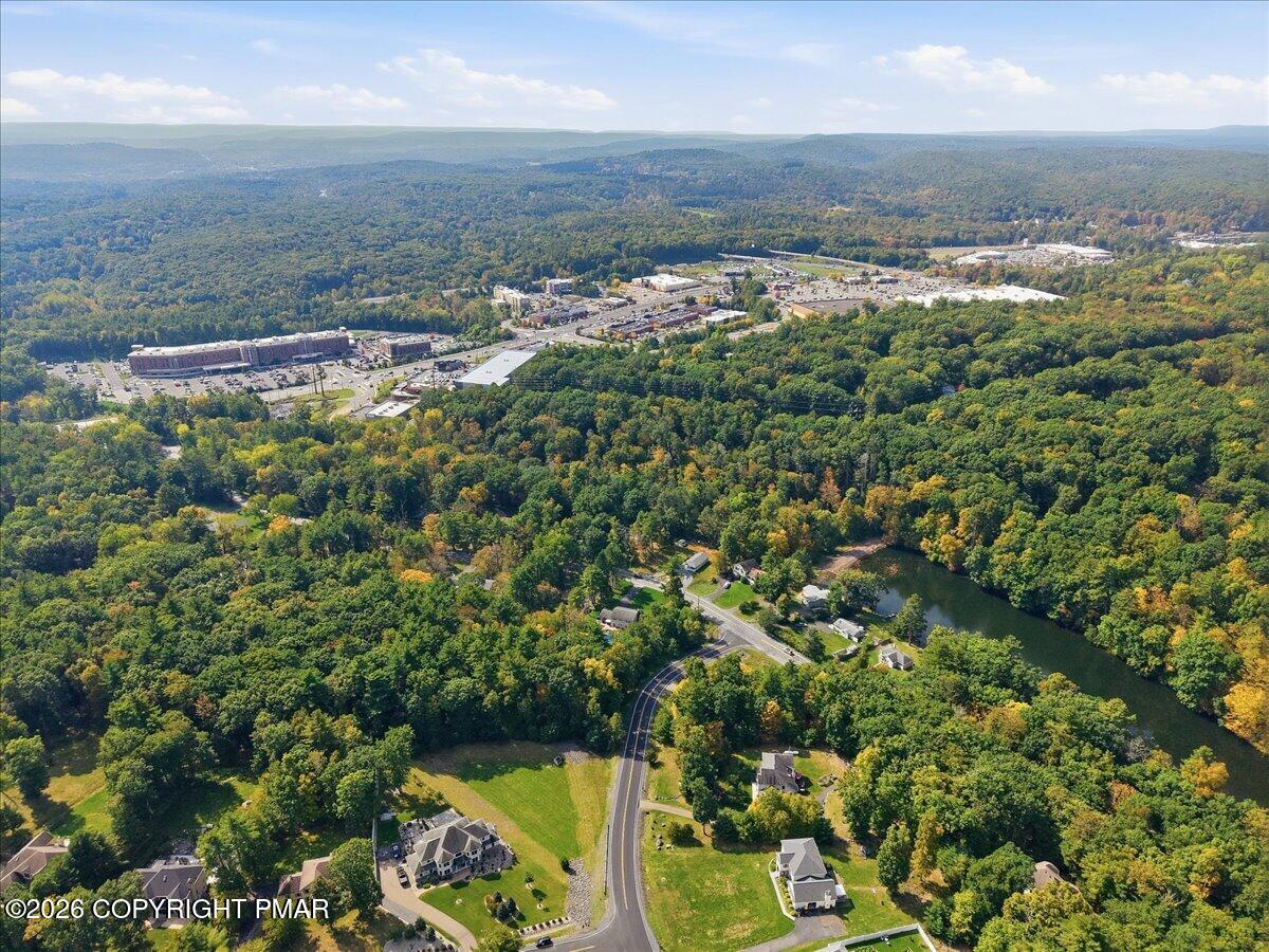Aerial view of wooded surroundings with scattered homes, a pond, and commercial buildings in the distance.