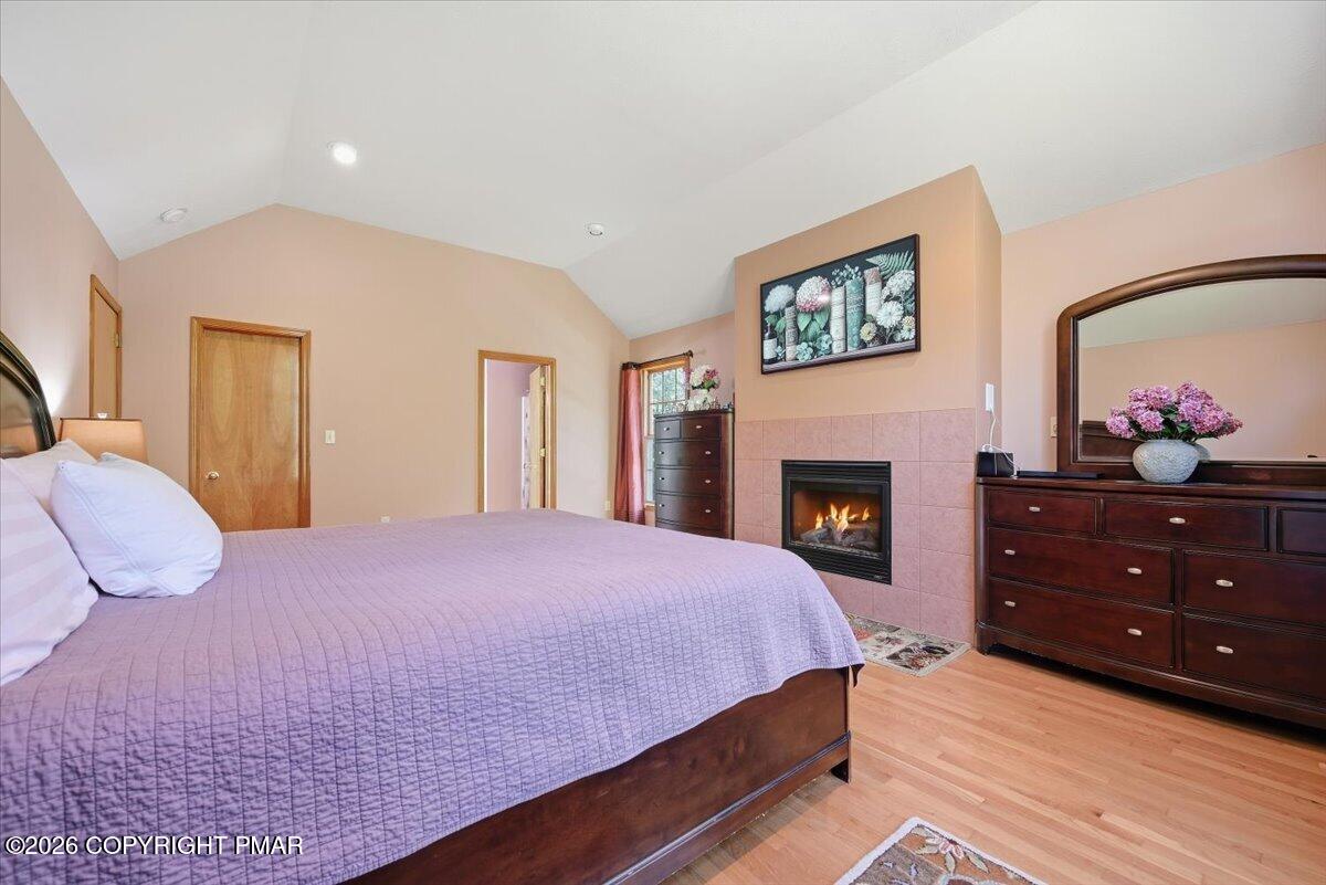 Bedroom with a lavender-covered bed and a tiled fireplace with a lit fire.