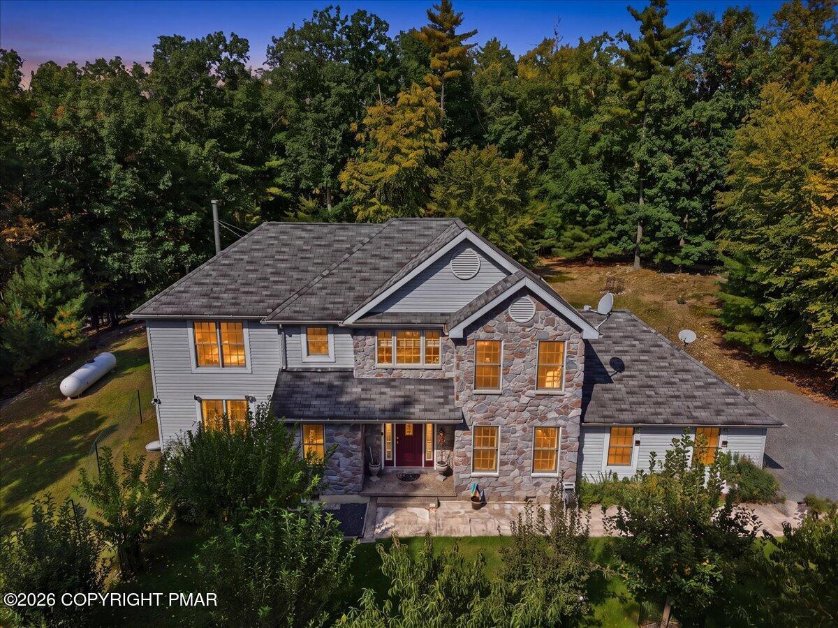 Aerial front view of a stone-and-gray-sided home with a red entry door, surrounded by mature trees.
