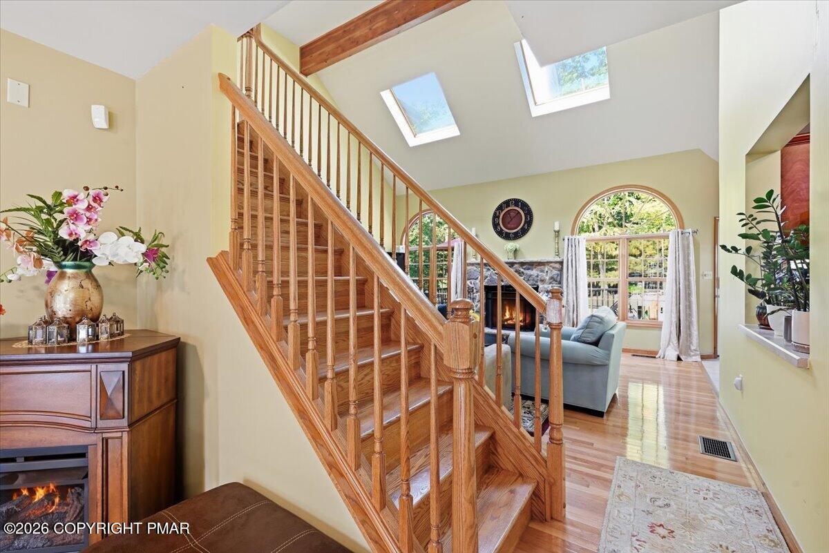 Wooden staircase in a bright foyer opening to a living room with skylights and arched windows.