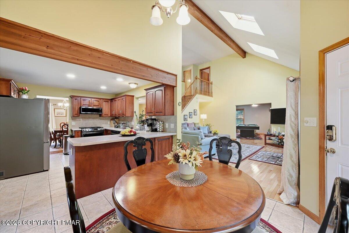 Open kitchen and dining area with vaulted skylit ceiling, wood beams, and adjoining living room.