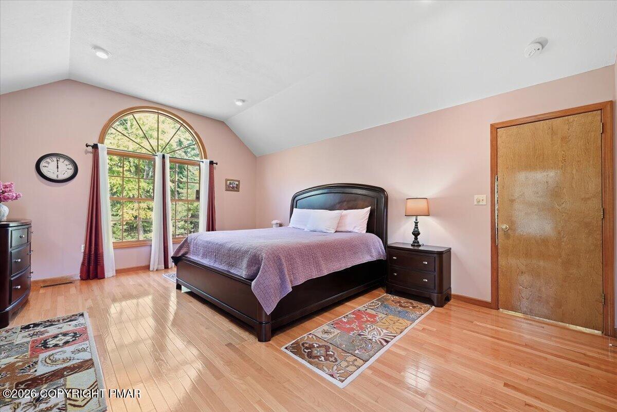 Bedroom with a vaulted ceiling, arched window, and dark bed on hardwood floors.