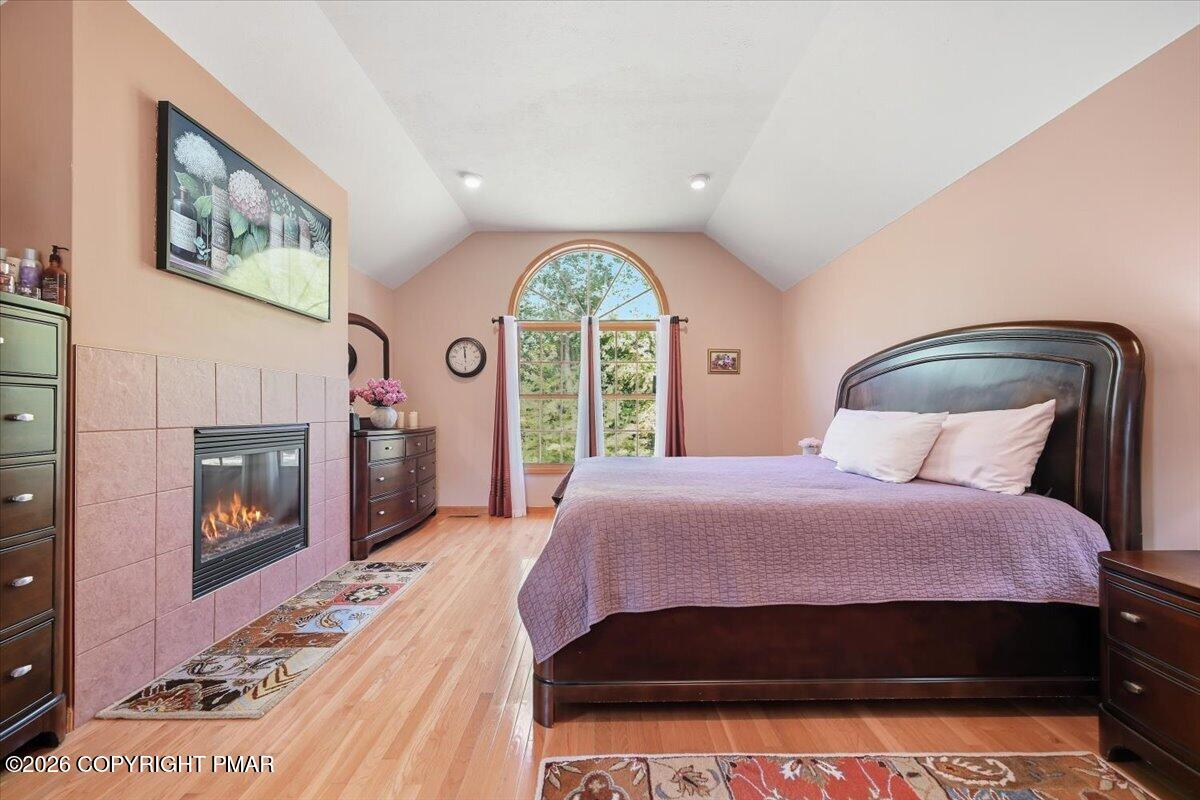 Bedroom with a vaulted ceiling, arched window, and tiled fireplace beside the bed.