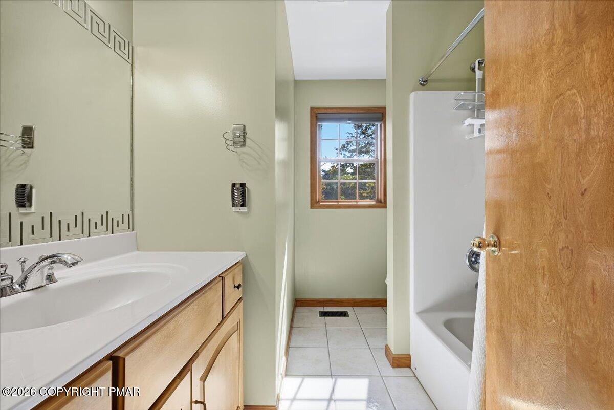 Bathroom with a wood vanity and large mirror, tiled floor, and bathtub beneath a shower.