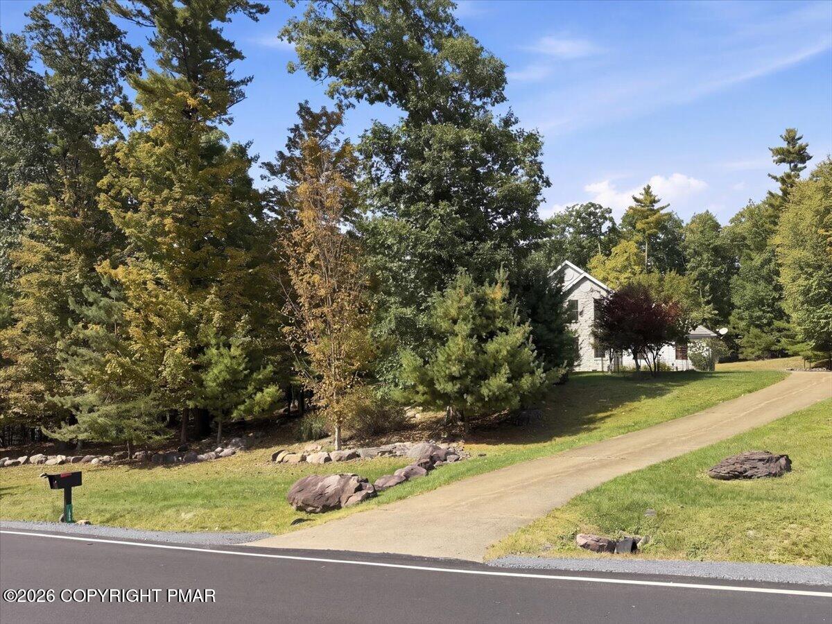 House partly screened by mature trees, with a sloped driveway and roadside mailbox.