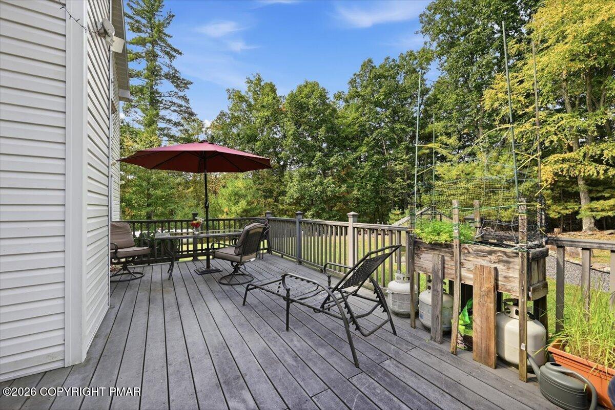 Wooden deck with lounge chairs, a burgundy umbrella, and raised garden beds beside the trees.