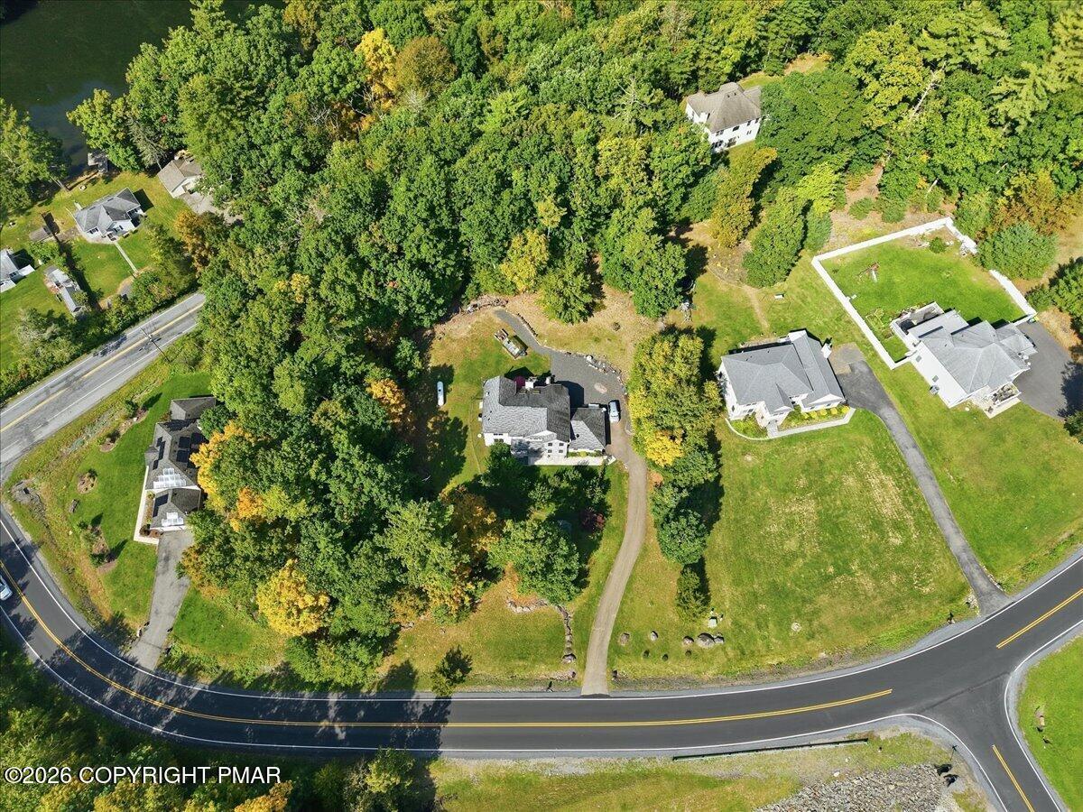 Aerial view of a tree-surrounded home and yard beside a curved road.