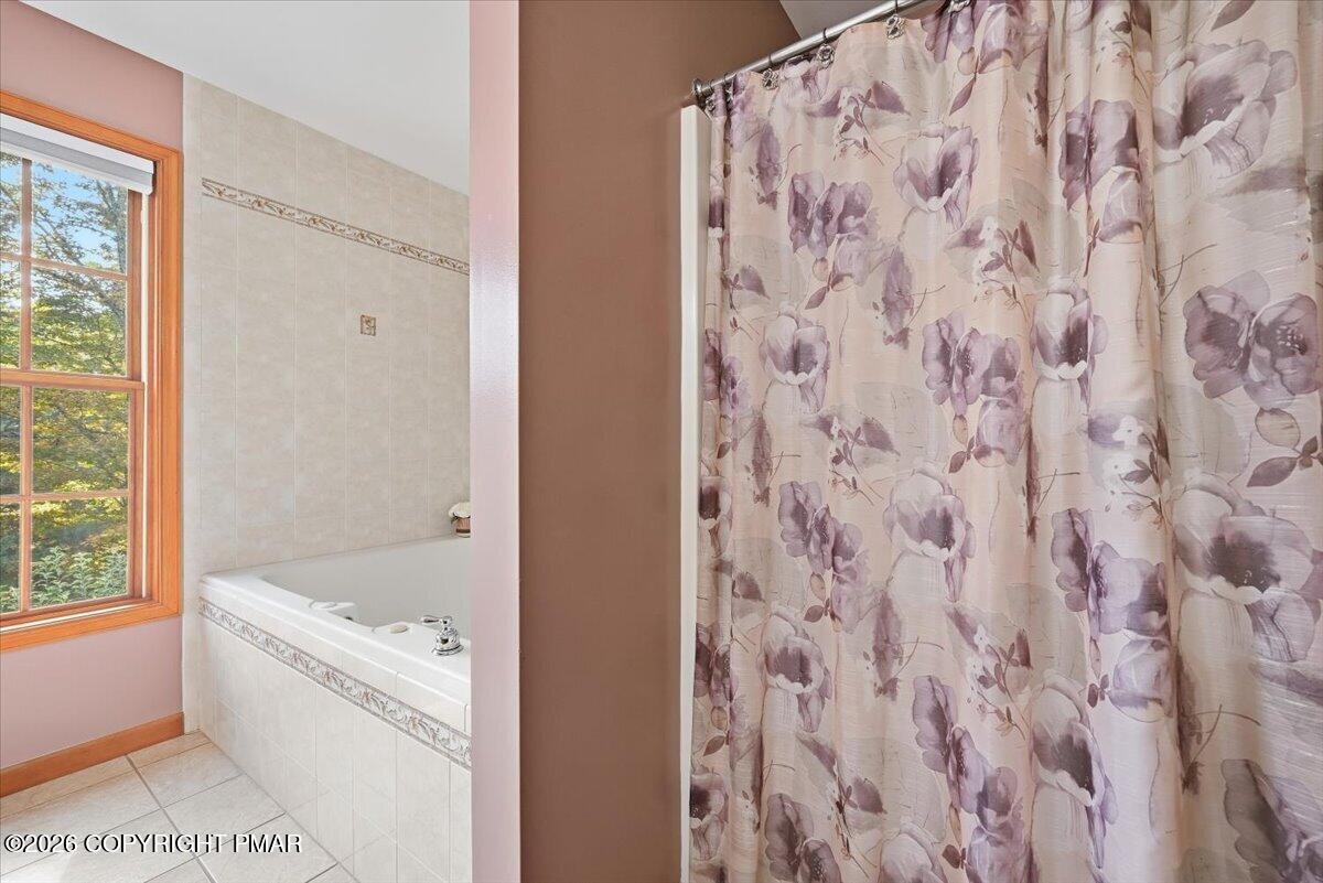 Bathroom with a tiled bathtub, wood-trimmed window, and floral shower curtain.