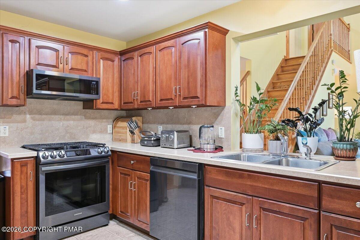 Kitchen with wood cabinetry, stainless steel appliances, and a sink beside a wooden staircase.