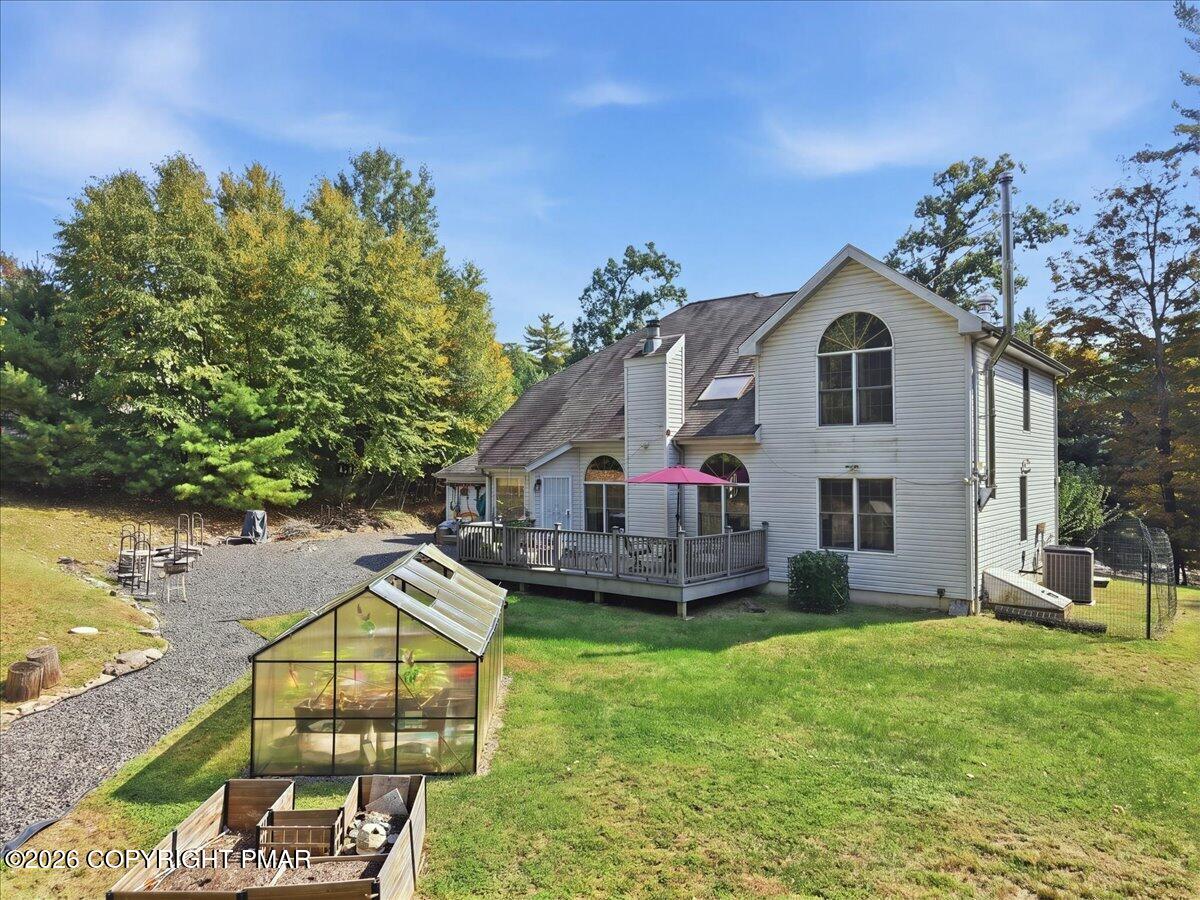 White two-story home with a raised deck, pink umbrella, and greenhouse in the backyard.