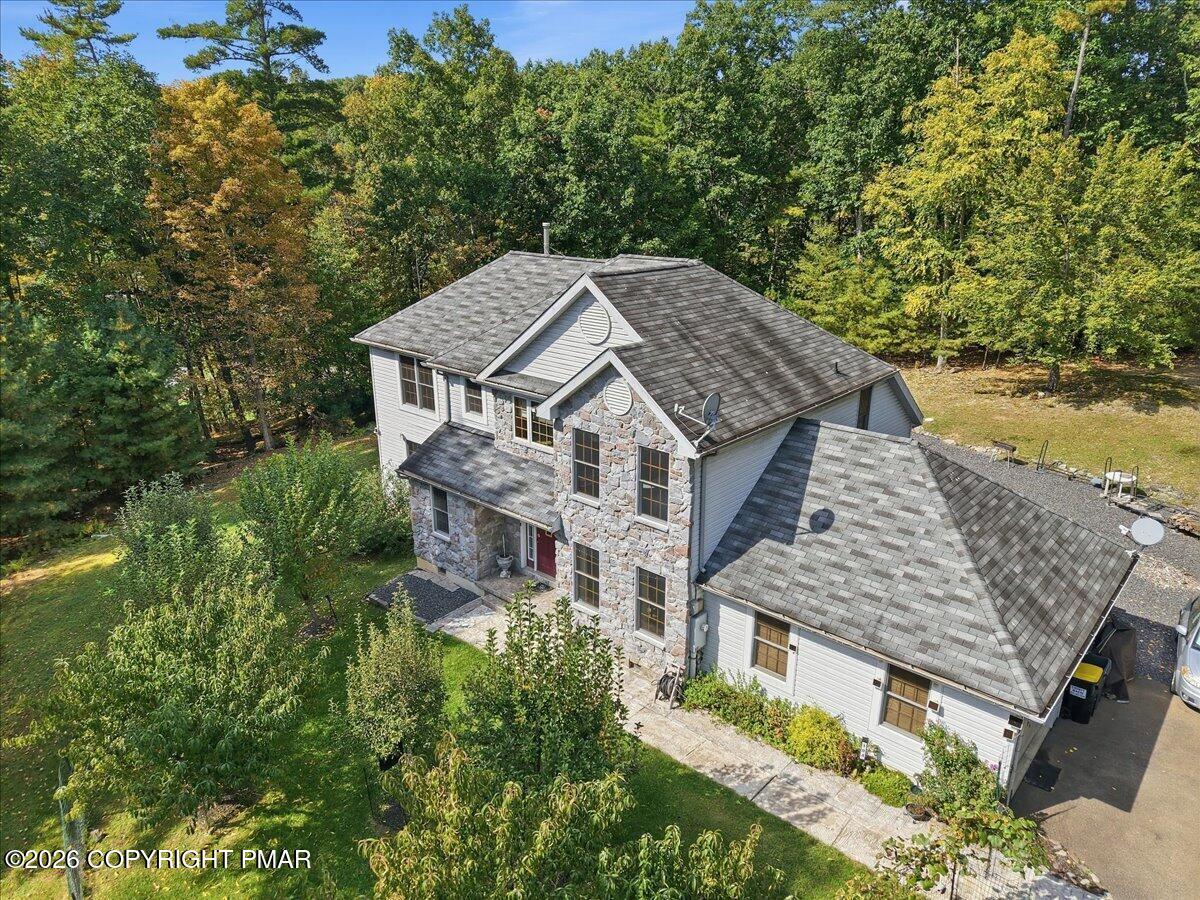 Aerial view of a stone-and-siding home with an attached garage amid a wooded lot.