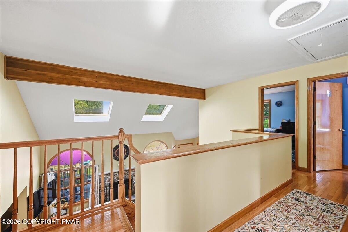 Upstairs landing overlooking a lower level, with a wood railing, exposed beam, and skylights.