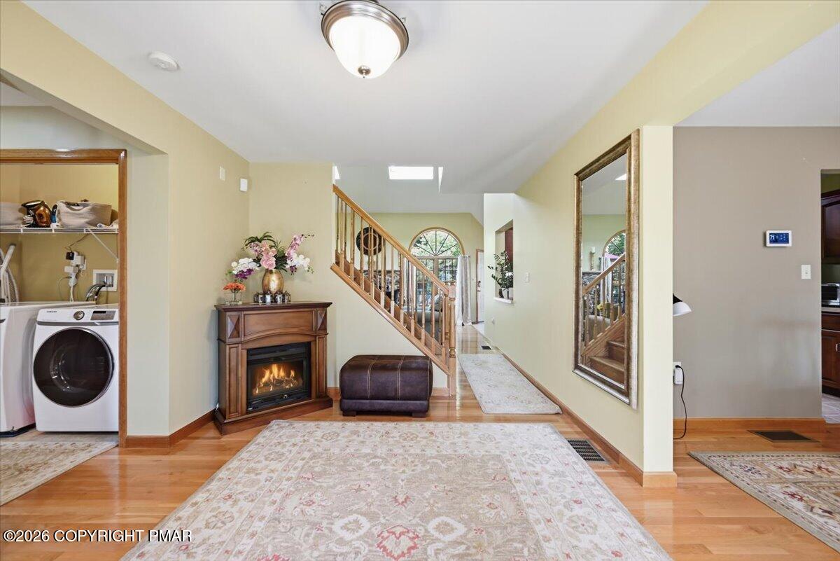 Entry hall with hardwood floors, staircase, fireplace, and a laundry nook with a front-loading washer.