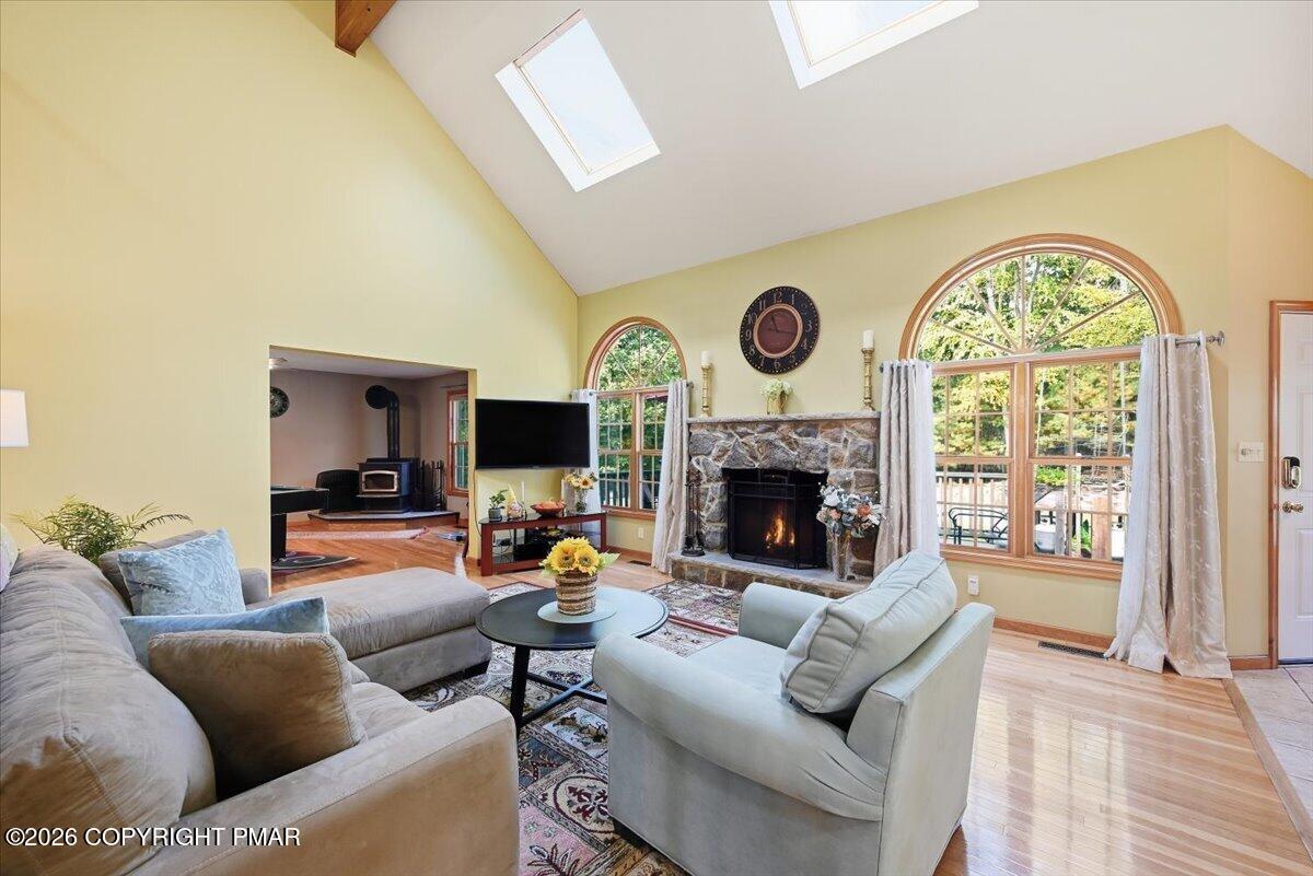 Living room with a vaulted ceiling, stone fireplace, skylights, and large arched windows.