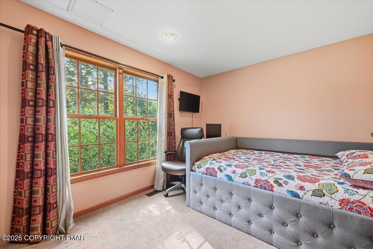 Bedroom with a gray upholstered bed and large wood-framed windows overlooking greenery.