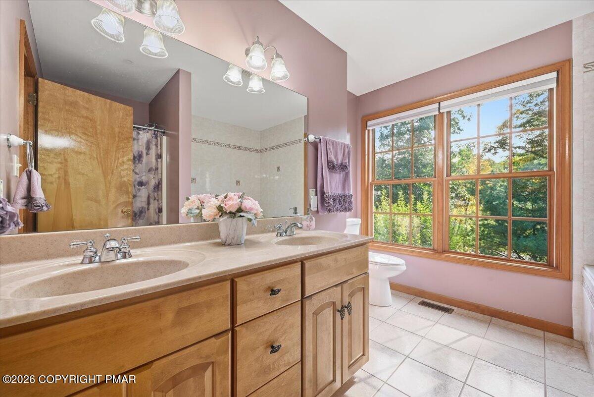 Bathroom with a double-sink wood vanity and a wide window overlooking trees.