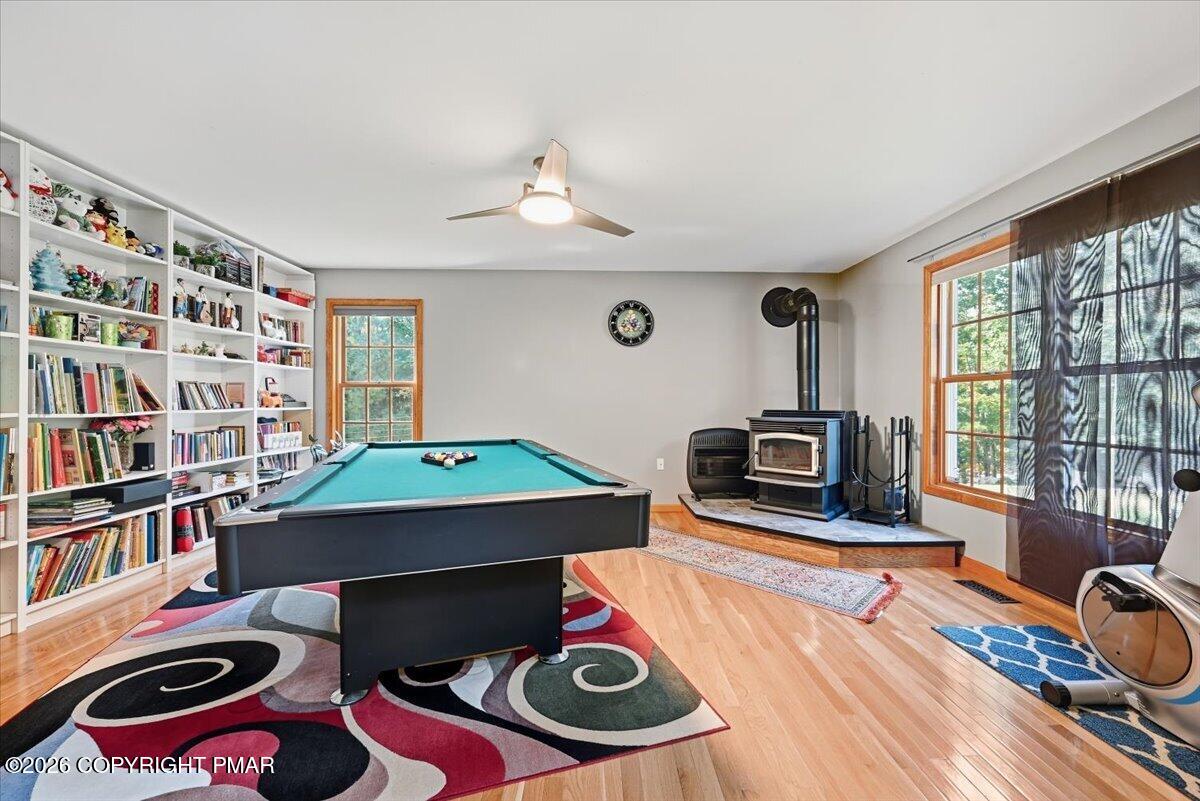 Game room with a teal pool table, wall-length bookshelves, and a freestanding wood stove.