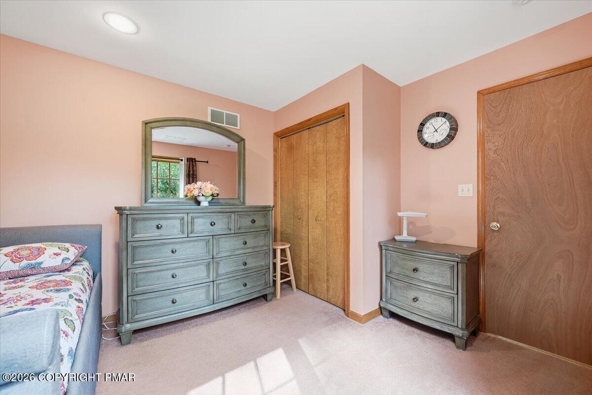 Bedroom with peach walls, gray dressers, a wood closet door, and sunlight across the carpet.
