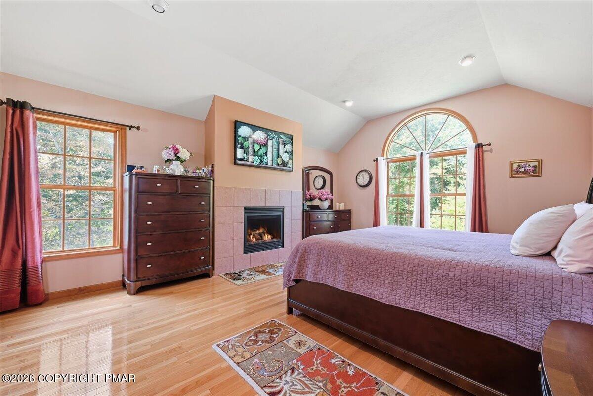 Bedroom with a tiled fireplace, hardwood floors, and a tall arched window.
