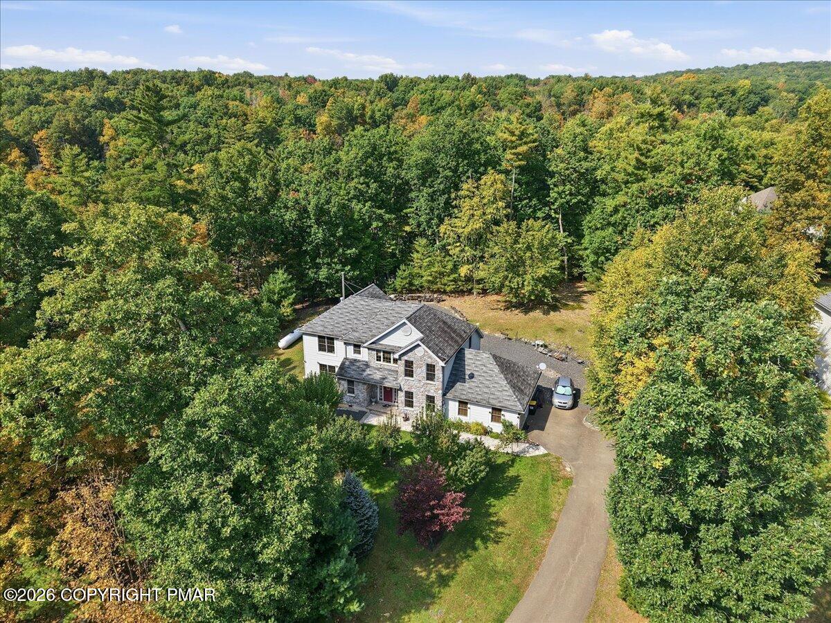 Aerial view of a two-story home surrounded by wooded grounds and a curving driveway.