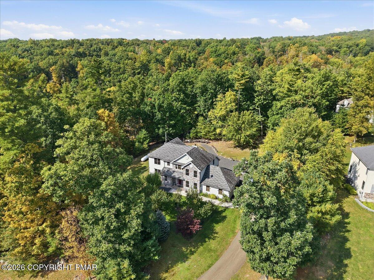 Aerial view of a house and driveway amid dense woodland, with early autumn colors in the trees.