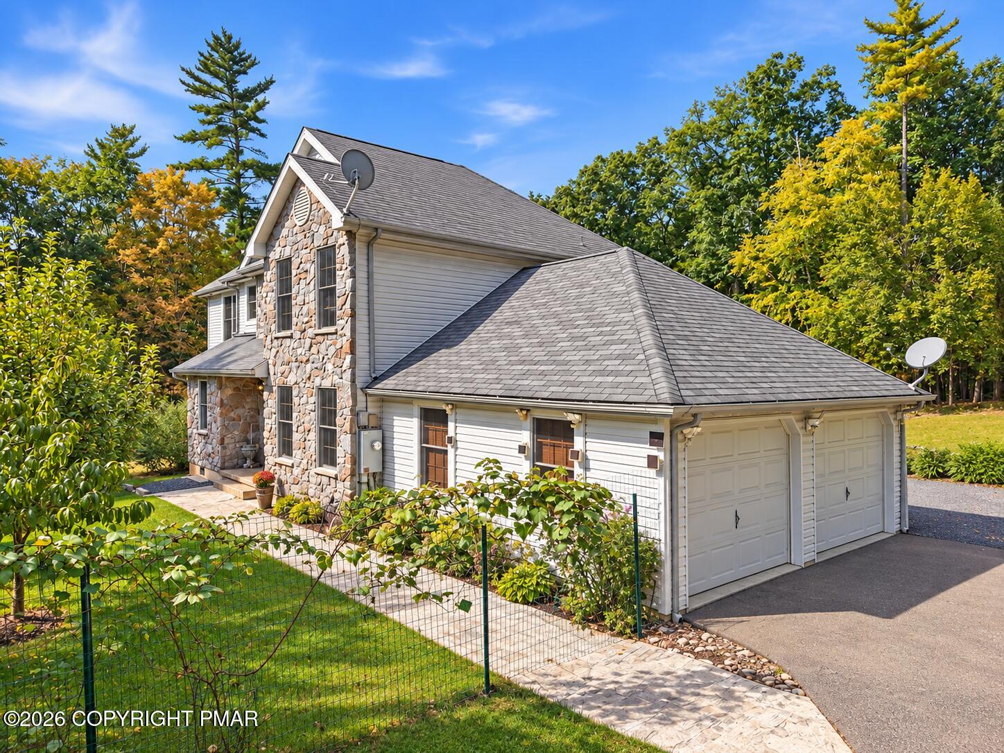 Two-story stone-and-siding house with an attached garage and fenced landscaped yard.