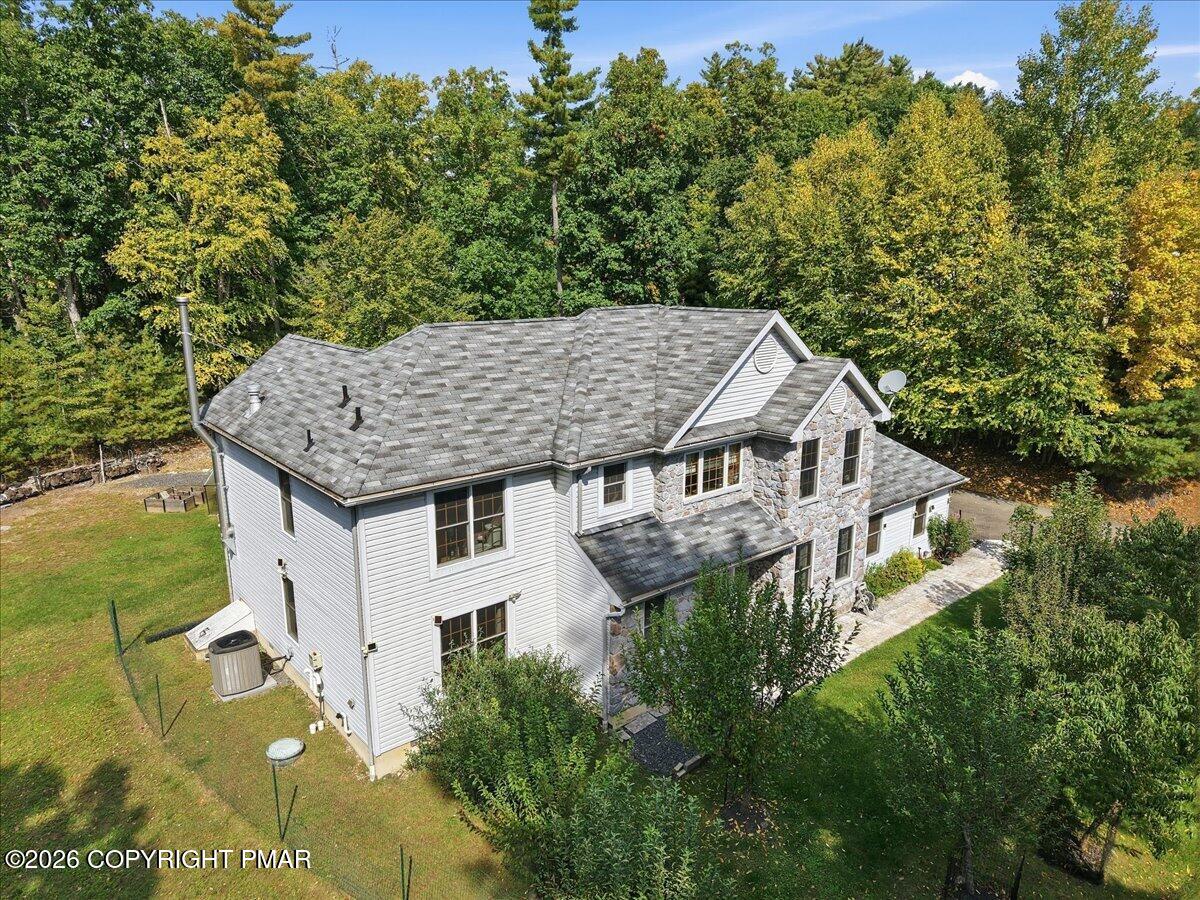 Aerial view of a gray-sided, stone-accented home surrounded by a lawn and autumn trees.