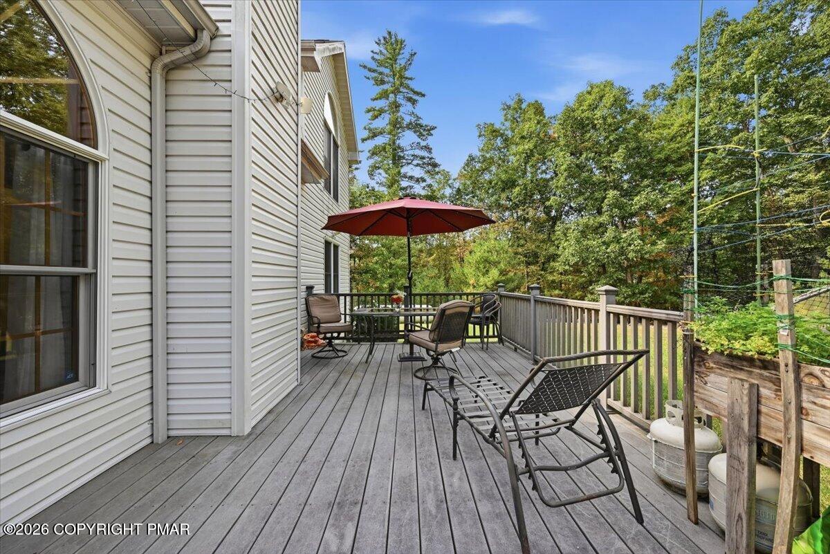Furnished deck beside a light-colored house, with black patio chairs and a red umbrella.
