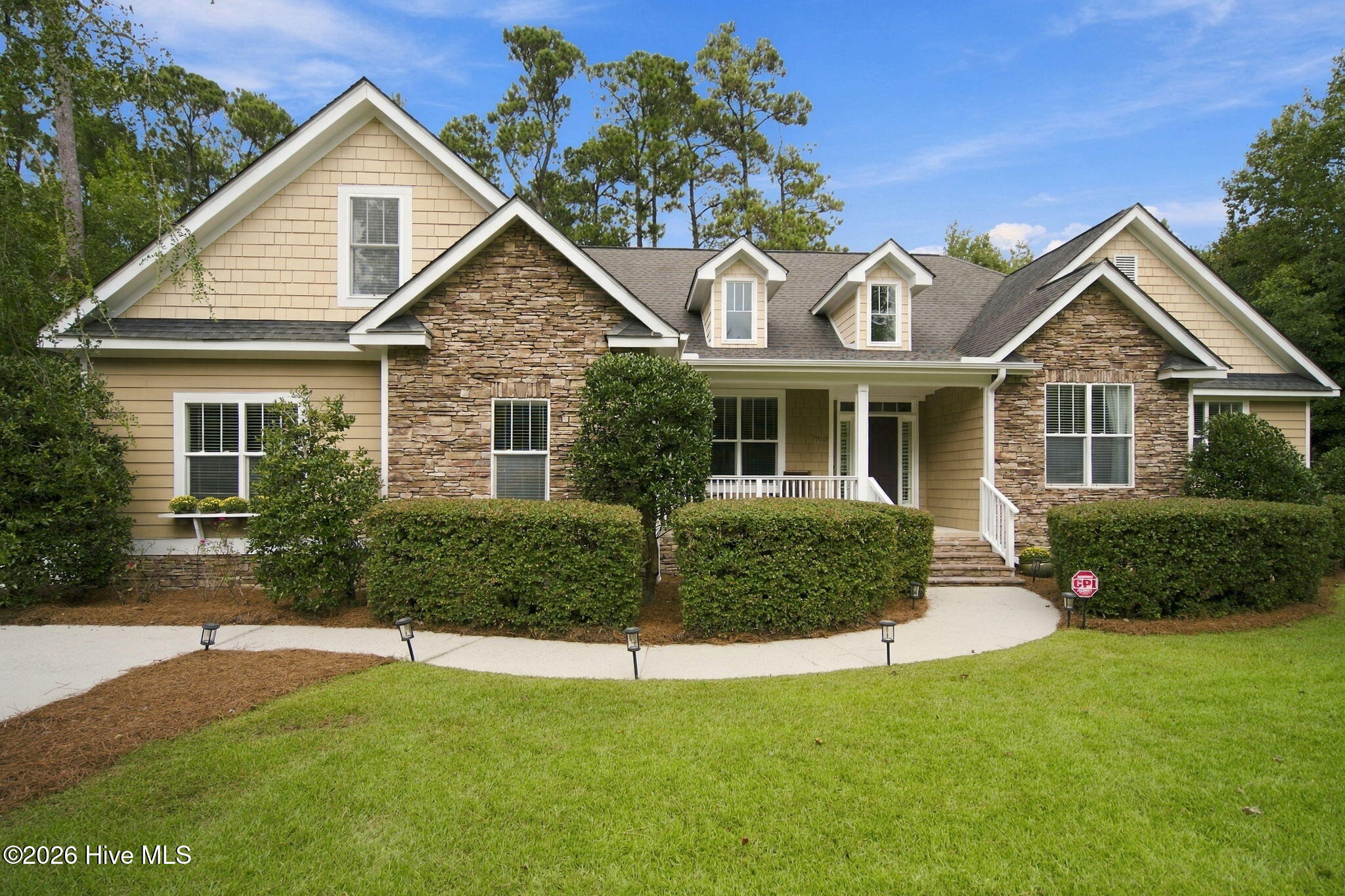 Beige house with stone accents, multiple gables, a covered porch, and neatly trimmed hedges.
