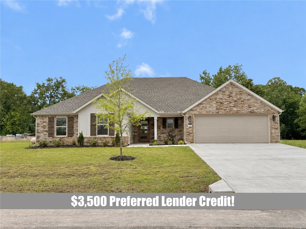 Single-story brick house with a two-car garage, broad driveway, and young tree in the lawn.